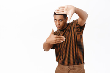 Wall Mural - Image of enthusiastic african american man taking picture, capture moment, looking through hand frames, white background