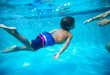 Young diverse boy swimming underwater in a swimming pool. Learning to swim with the help of his parent. Photo below the water showing a child practicing diving under the water