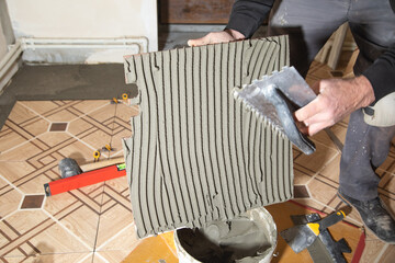 Wall Mural - Worker using spatula and putting glue on ceramic tile.