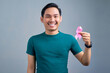 © Bangun Stock Photo - Close-up of young Asian man wearing white t-shirt holding pink ribbon breast cancer symbol or keeping HIV disease awareness, healthcare, medicine concept.