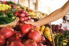 Woman Choosing Pomegranate Among Many Others While Having Great Food Shopping At The Local Food Market. Stock Photo. High Quality Photo