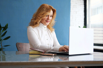 Wall Mural - Beautiful mature business woman blonde sitting at a laptop in the office and typing