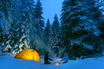 Wall Mural - couple camping with campfire and tent outdoors in winter forest