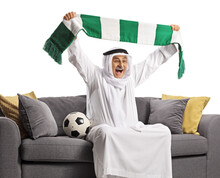 Cheerful Arab Man Cheering With A Scarf And Sitting On A Sofa With A Football