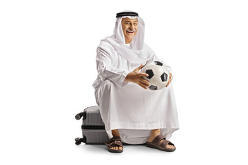 Sticker - Smiling mature arab man in ethnic clothes sitting on a suitcase and holding a football