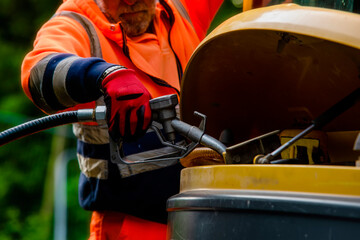 Builder in safety gloves filling excavator with diesel fuel on building site