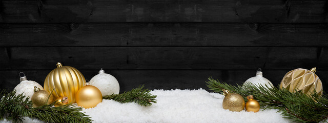 Festive ornaments advent celebration holiday holidays banner greeting card - Golden and white christmas baubles, christmas balls and pine branches on snow, with black wooden wall in background