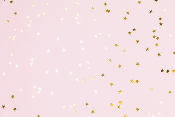 Gold sparkle confetti stars on a pink pastel background. Glitter, shine, bright. Christmas festive flat lay, winter holiday, new year, happy birthday concept. Flat lay, top view, copy space.