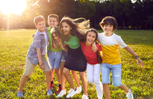 Group Of Happy Cheerful Active Little Children Enjoying Summer Break, Meeting In Park, Frolicking On Green Grass, Playing Fun Games, Making New Friends, Hugging, Smiling And Having Great Time Together