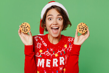 Wall Mural - Merry amazed fun young woman wear knitted xmas sweater Santa hat posing hold in hand chocolate biscuits isolated on plain pastel light green background Happy New Year 2023 celebration holiday concept