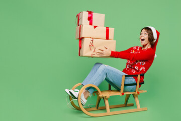 Wall Mural - Full body side view merry young woman wear knitted xmas sweater Santa hat posing sledding hold gift present boxes isolated on plain pastel light green background. Happy New Year 2023 holiday concept.