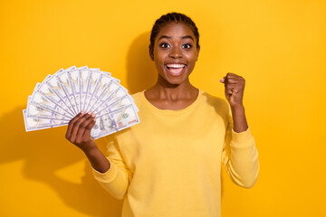 Wall Mural - Portrait of beautiful trendy cheerful lucky girl holding banknotes us atm cash rejoicing isolated over bright yellow color background