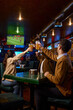 © Nomad_Soul - Friends watching football match clinking beer mug rest in sport bar