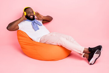 Wall Mural - Full body photo of young guy relaxing in beanbag listen favorite music genre in headset isolated on pink color background