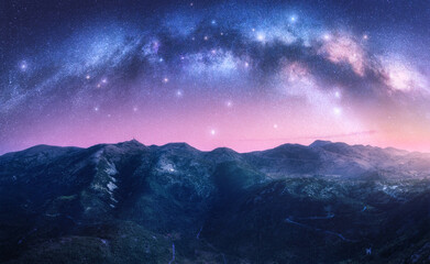 Wall Mural - milky way arch over the mountains at starry night. pink sky with bright stars and arched milky way i