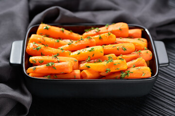 Wall Mural - Roasted baby carrots in a ceramic form on a dark wooden table. Healthy root vegetables concept.