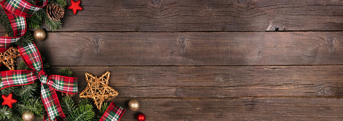 Wall Mural - Christmas corner border of ornaments, branches and red and green plaid bows and ribbon. Top down view on a rustic wood banner background.