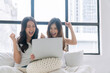© kaew6566 - Excited asian Lgbtq couple young woman watching movie or soccer online laptop sitting together on bed. Cheerful lesbian girl exciting success surprised looking website online on laptop. Domestic life.