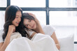© kaew6566 - Romantic asian lgbt couple woman sitting together wake up on white bed with pillow in morning at home. Lover lesbian young girl hugging together closeness relax beside window bedroom.Relationship lgbt