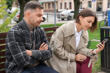 Distrustful Man Peering Into Girlfriend's Smartphone Outdoors. Relationship Problems