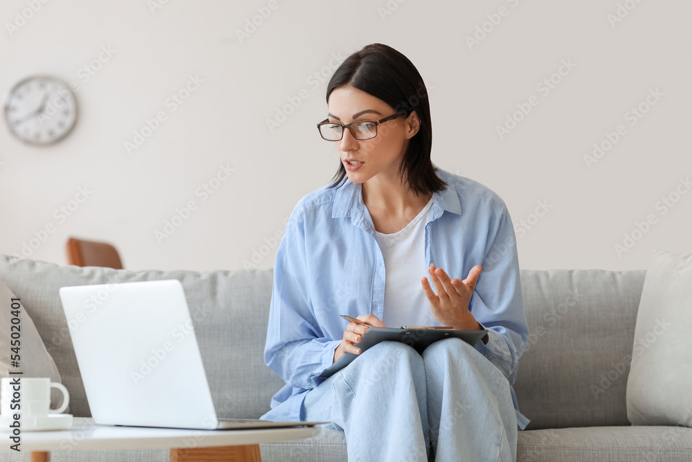 Female psychologist video chatting with patient on sofa at home