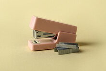 Pink office stapler and staples on color background