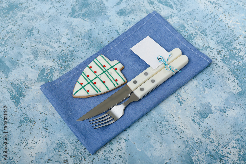 Napkin with cutlery and Christmas cookie on color background