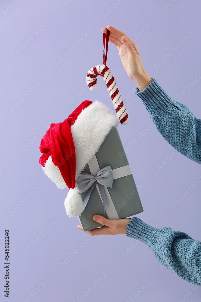 Woman with Christmas gift box and candy cane on lilac background