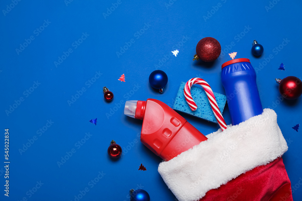 Santa hat with cleaning supplies and Christmas decor on blue background