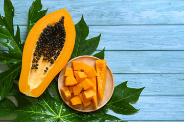 Wall Mural - papaya fruits on blue backgroud, fresh ripe papaya slice cut in half tropical fruit with papaya seed and leaf leaves from papaya tree