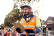 © Austockphoto - man road worker with beard wearing white hat and orange and yellow jacket holding his notes