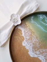 Epoxy Resin Sea Wave In Serving Round Brass Tray , Resin Beach. White Napkin In A Orchid Ring. Top View, Table Setting. 