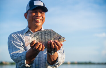 Wall Mural - Aquaculture farmer man showcasing quality-raised tilapia in his hands