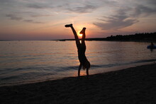 Silhouette Woman Handstanding At Beach Against Sky During Sunset