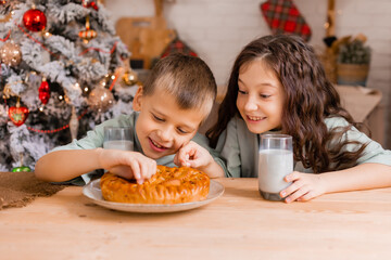 two small children a boy and a girl eat Christmas cake with milk in the morning at home in the kitchen