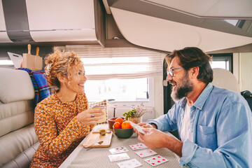 One happy couple enjoy time and have fun together inside camper van during travel lifestyle or holiday with vehicle. Man and woman playing cards with smile and joy.. Indoor leisure activity people