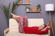 Portrait of happy delighted satisfied woman wearing red sweater and checkered pants lying on sofa in home interior and having rest after hard working day, enjoying weekend.
