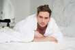 © Евгений Шемякин - Portrait of handsome sleepy lazy nice man, young guy lying in bedroom in bed covering himself with white blanket, smiling looking at camera at early morning. Laziness, procrastination weekend day.