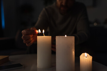 Wall Mural - partial view of man lighting candles near mobile phone on table during electricity outage.