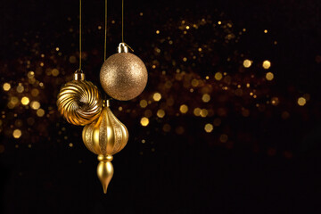 christmas card with three golden balls decorations on black background with bokeh lights
