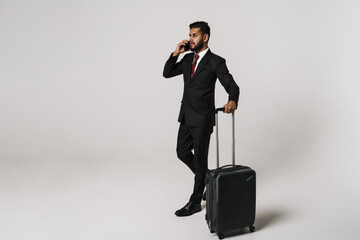 Young indian man talking on cellphone while walking with suitcase