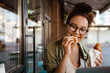 © Drobot Dean - White young woman eating croissant while using laptop in cafe outdoors