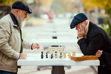 Portrait Of Two Senior Men Playing Chess In The Park On A Daytime In Fall. Thoughtful Activity. Concept Of Leisure Activity, Old Generation