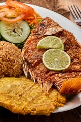 Canvas Print - Vertical top view of a white plate with Pescado Frito, rice, and a vegetable salad on a wooden table