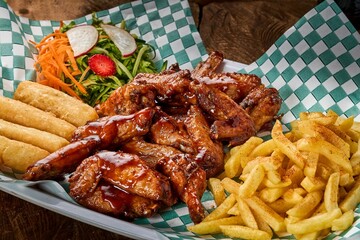 Sticker - Top view of fried chicken wings, vegetable salad, and potatoes on a plate on a wooden background