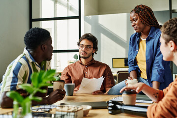 Wall Mural - Young confident manager with papers talking to African American male colleague during coffee break while preparing for seminar