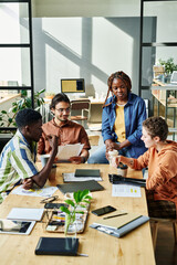 Wall Mural - Group of young employees gathered by table in office to have coffee and discuss some working points concerning new business project