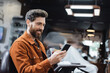 © LIGHTFIELD STUDIOS - happy bearded man using mobile phone in blurred barbershop.