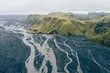 Aerial shot of a river flowing trough the green-covered mounts in the Katla Geopark, Iceland
