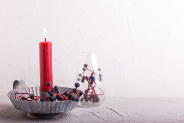 Wall Mural - Simple postcard with  red burning candle, white roses and blue wild berries on light background. Selective focus. Still life. Romantic postcard. Place for text.